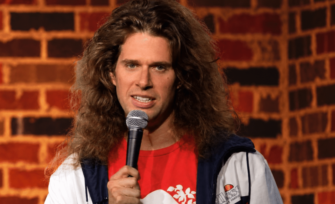 John Jacobs performing stand-up in front of a brick wall