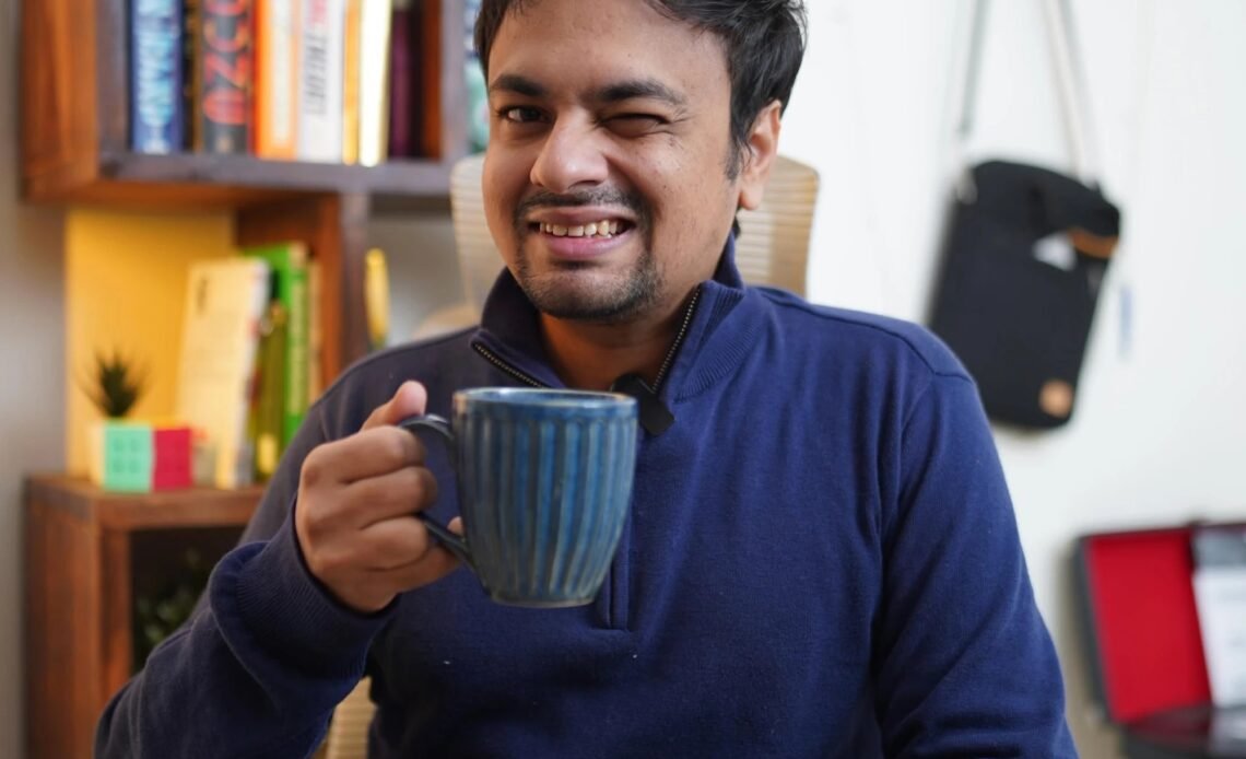 Kishan of Hop For Pop smiling and winking while holding a blue mug